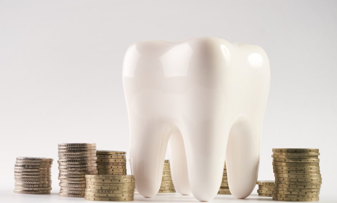 A white tooth next to several piles of coins